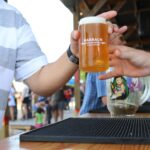 Two people exchange a freshly poured beer outdoors by the bar counter.